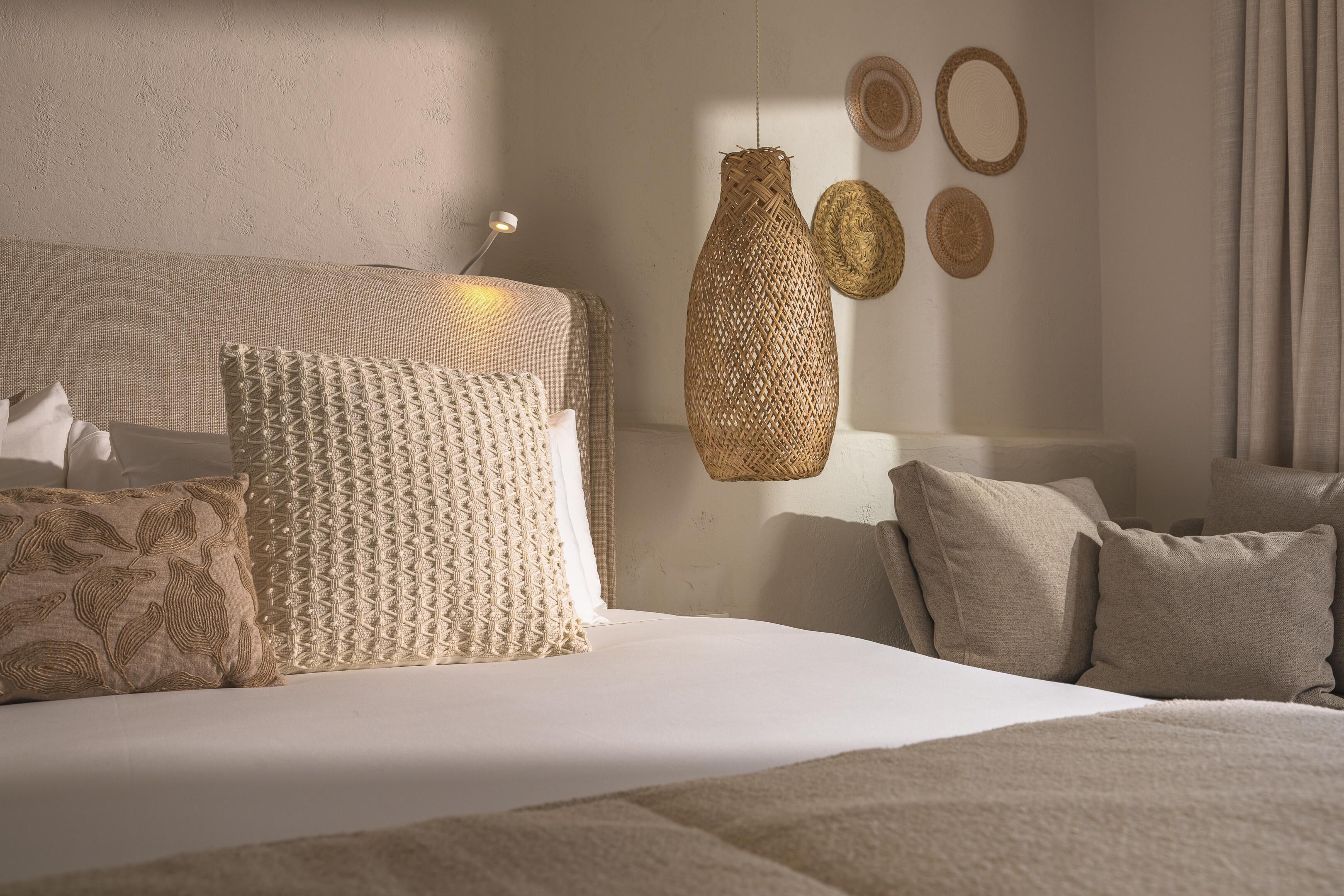 Camera da letto ordinata con un letto grande, numerosi cuscini, un lampadario intrecciato e decorazioni murali in tessuto.
