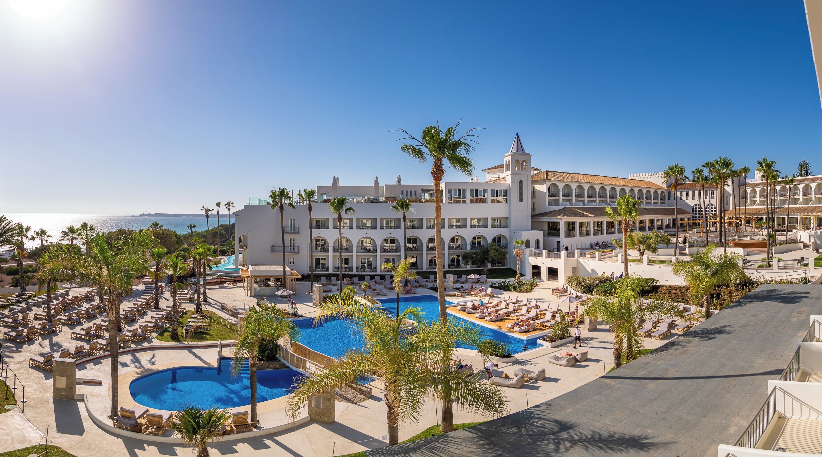 Un resort con una piscina grande, palmeras y vista al océano.