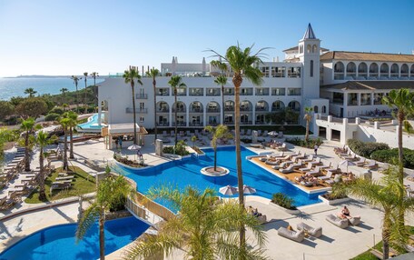 A resort with a large pool, multiple balconies, and a view of the sea.