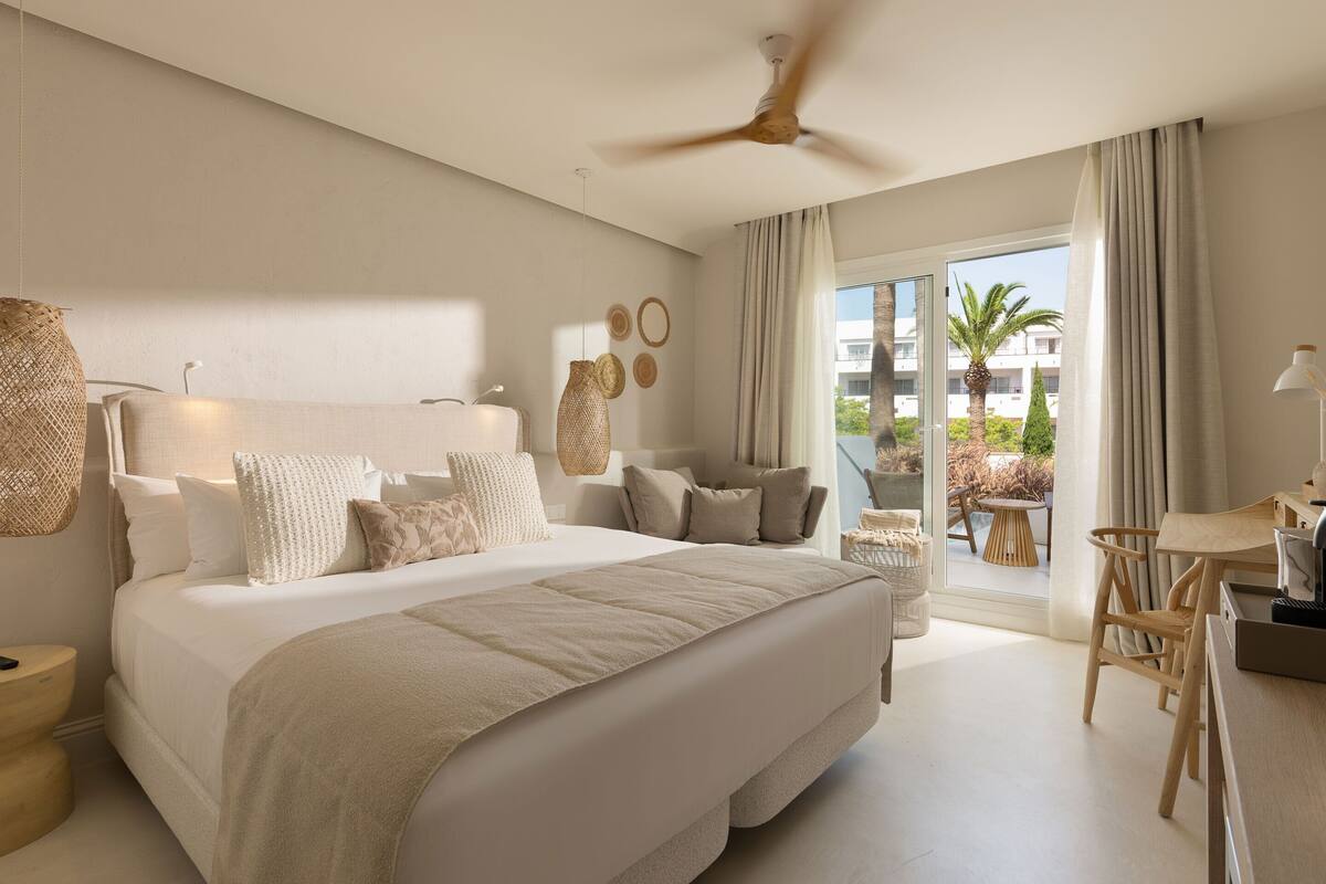 A spacious bedroom with a large bed, a ceiling fan, and a view of the outdoor balcony.