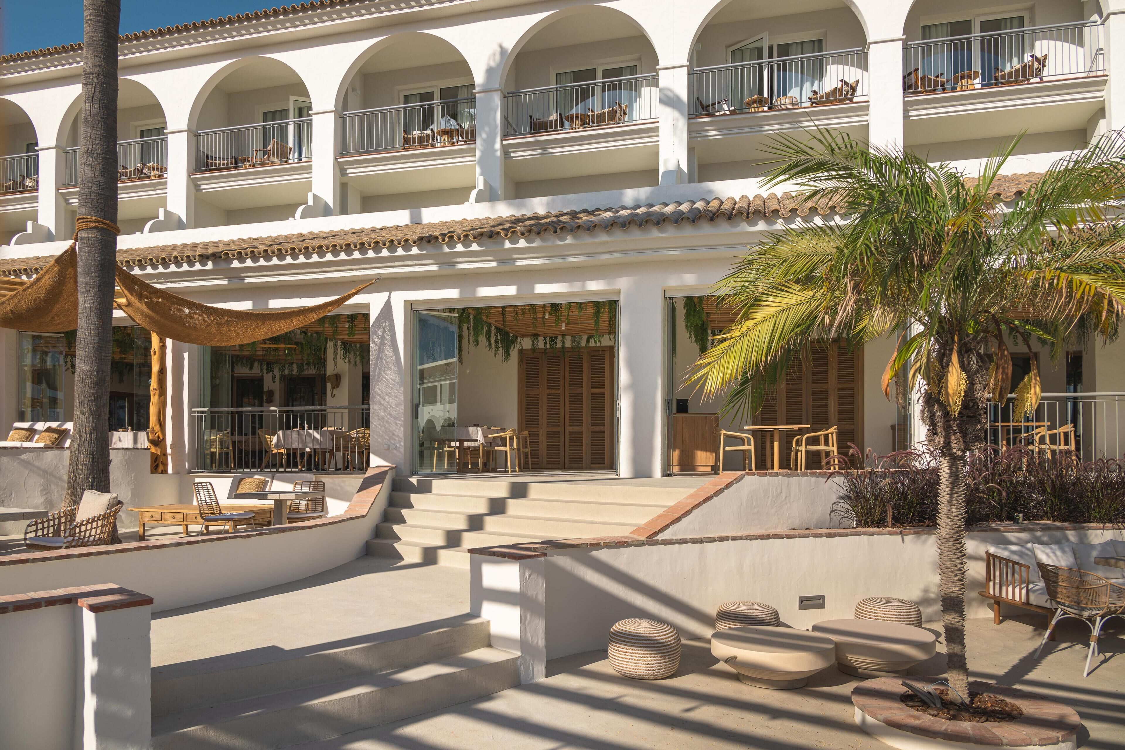 A hotel with a courtyard featuring outdoor seating, palm trees, and a staircase leading to the upper floors.
