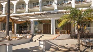A hotel with a courtyard featuring outdoor seating, palm trees, and a staircase leading to the upper floors.