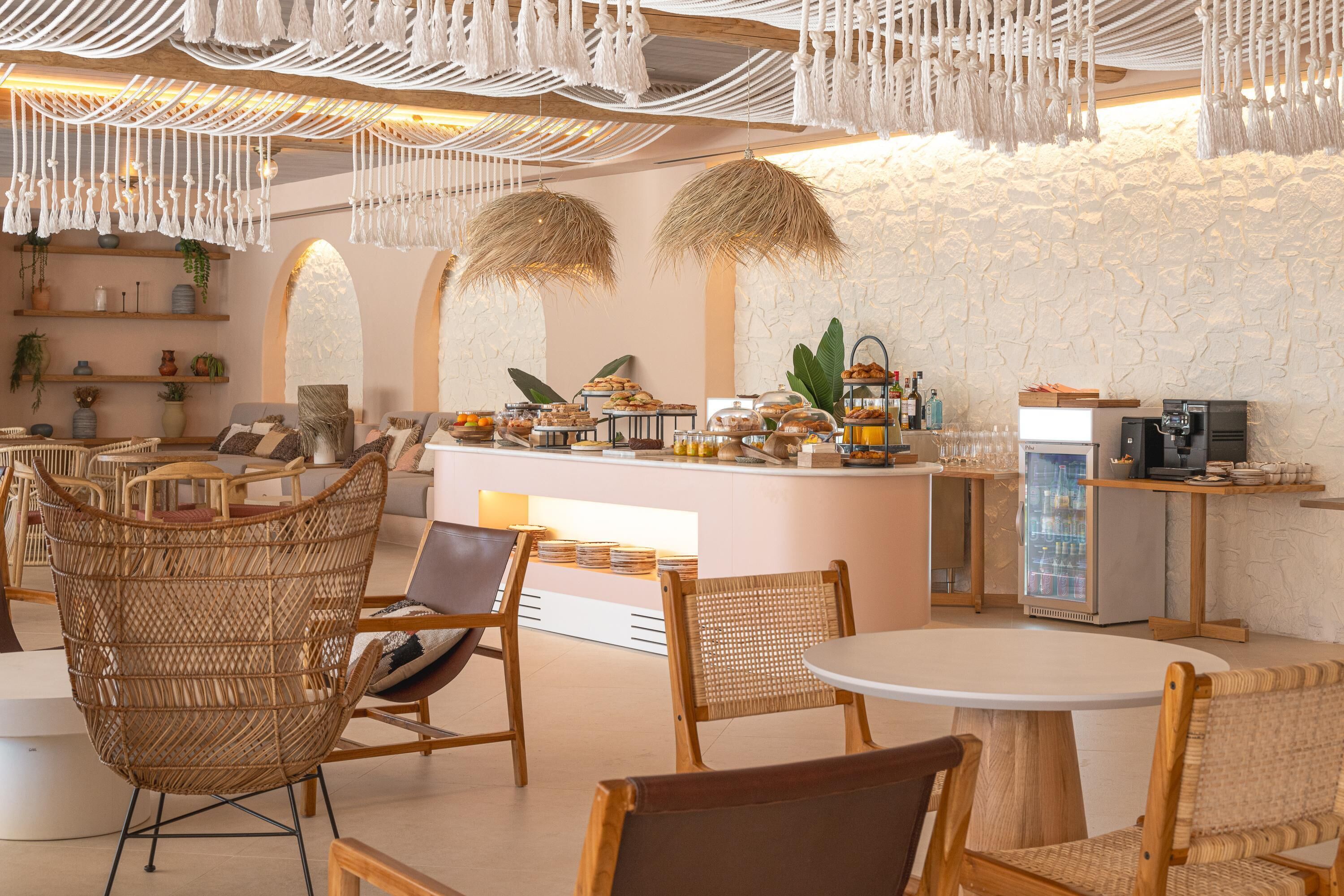 A cozy cafe with wicker chairs, a central island with food and drinks, and a stone wall backdrop.