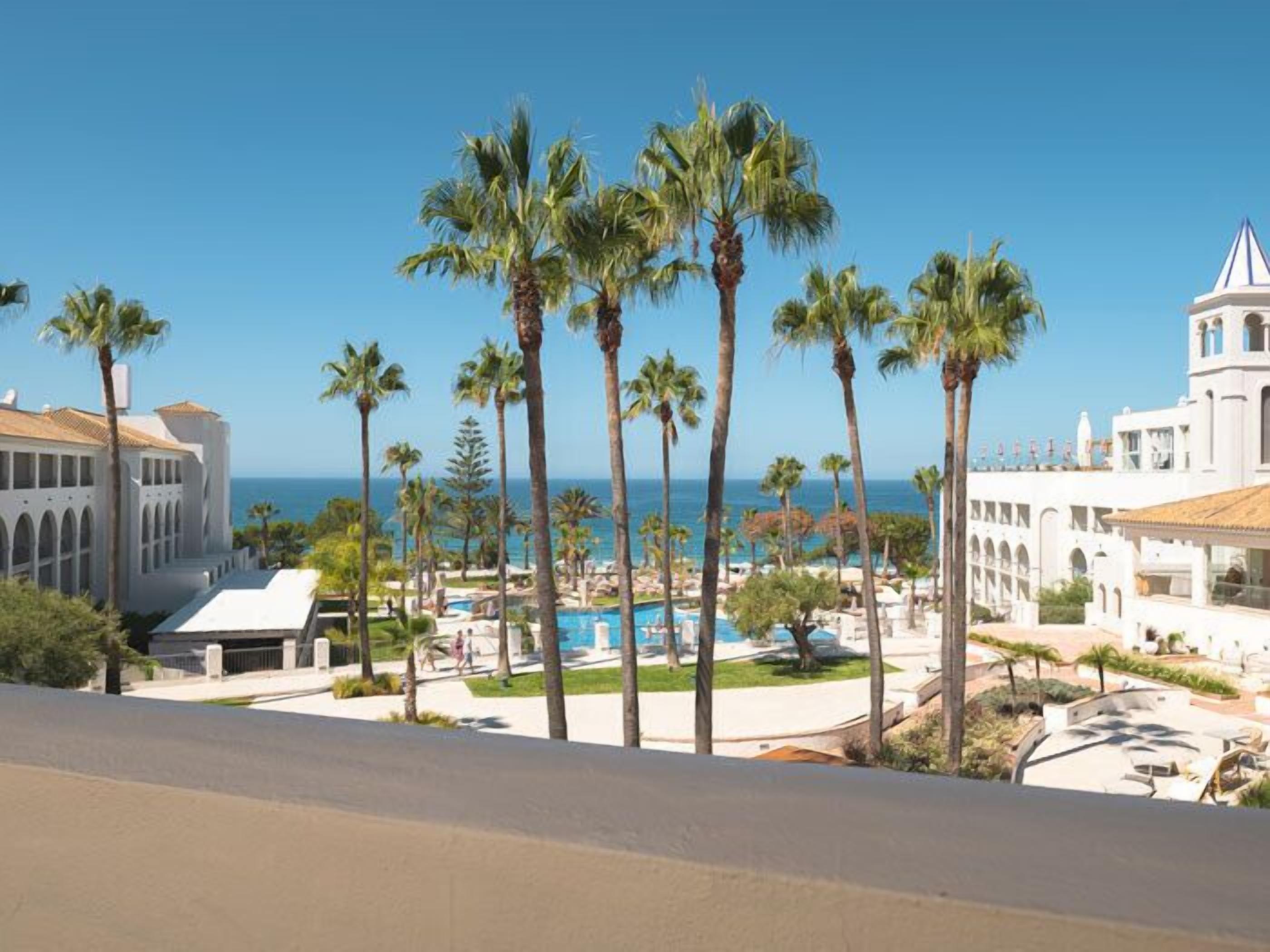 A resort with a pool, palm trees, and a view of the ocean.