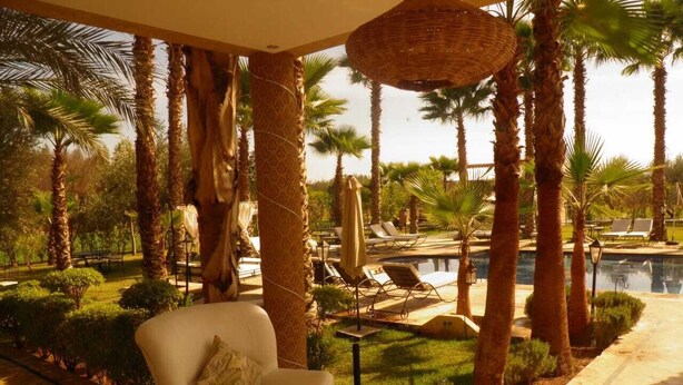 A poolside lounge area with a white sofa, a small table, and a wicker umbrella. - The les deux palmiers Marrakech Complex (Marrakech)