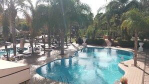 A pool area with lounge chairs and umbrellas, surrounded by palm trees and a building in the background. - The les deux palmiers Marrakech Complex (Marrakech)