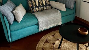 A teal sofa with multiple cushions, a woven rug, and a small black table with a bowl.