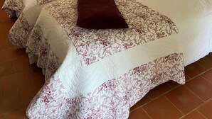 A double bed with floral bedding and two pillows, a bedside table with a lamp, and a striped curtain.
