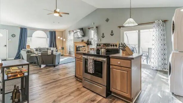 A modern kitchen with wooden cabinets, a built-in oven, and a dining area with a table and chairs. - Belle of the Chesapeake Bay (Lusby)