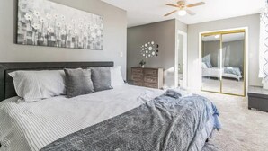 A bedroom with a large bed, a ceiling fan, a wall-mounted artwork, a dresser, and a sliding glass door leading to another room. - Belle of the Chesapeake Bay (Lusby)