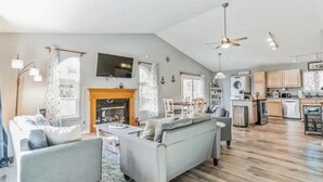 A spacious living area with a fireplace, a sofa, and a kitchen in the background. - Belle of the Chesapeake Bay (Lusby)