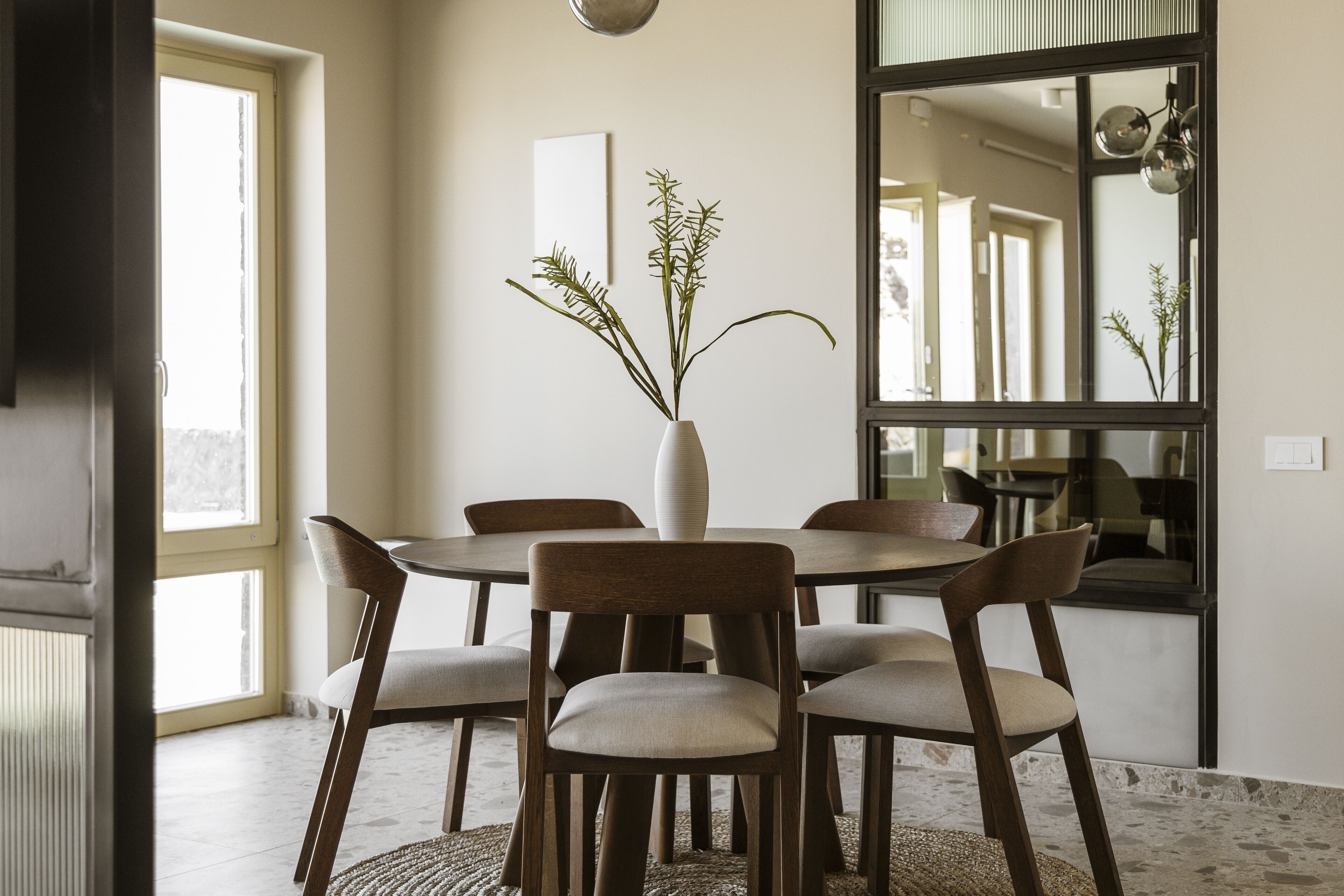 A dining area with a round table, six chairs, and a vase with plants.