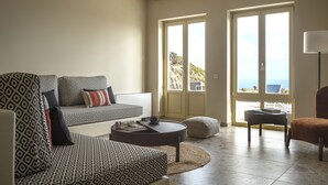 A living room with patterned furniture, a round coffee table, and a view through a door. - Almarossa Villas (Santorini)