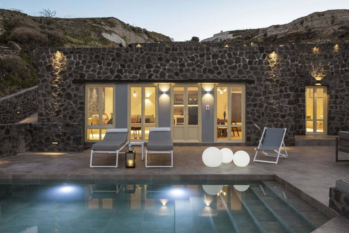 A stone building with a pool, lounge chairs, and a dining area.