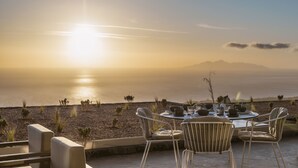 A terrace with a table set for dining, overlooking a beach and the sea. - Almarossa Villas (Santorini)