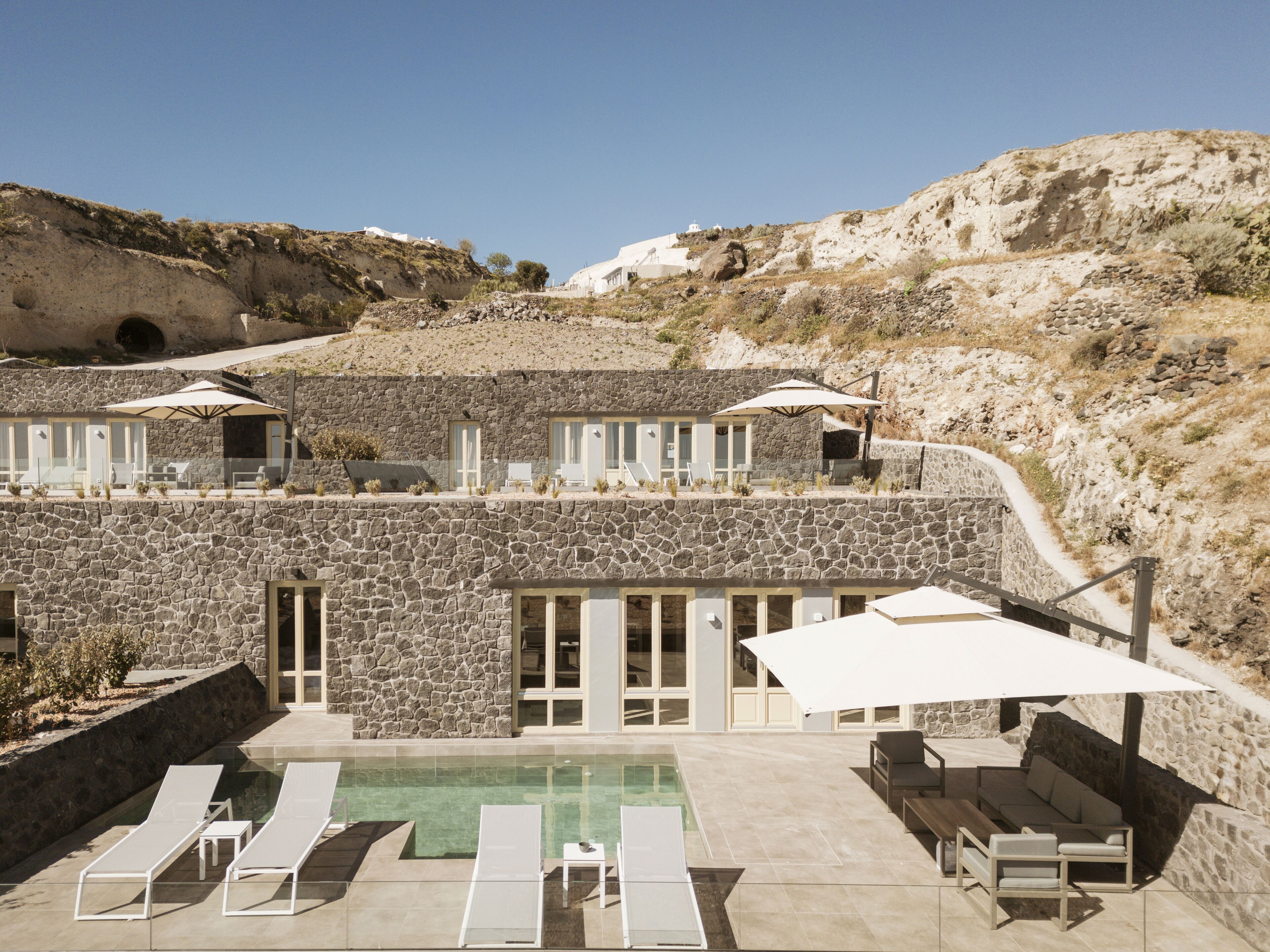 Un bâtiment en pierre doté d’une piscine, de chaises longues et d’un espace salon extérieur.
