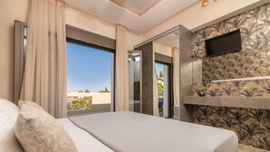 A bedroom with a large bed, a TV mounted on the wall, and a balcony with a view. - Lazai Villa (Zakynthos)