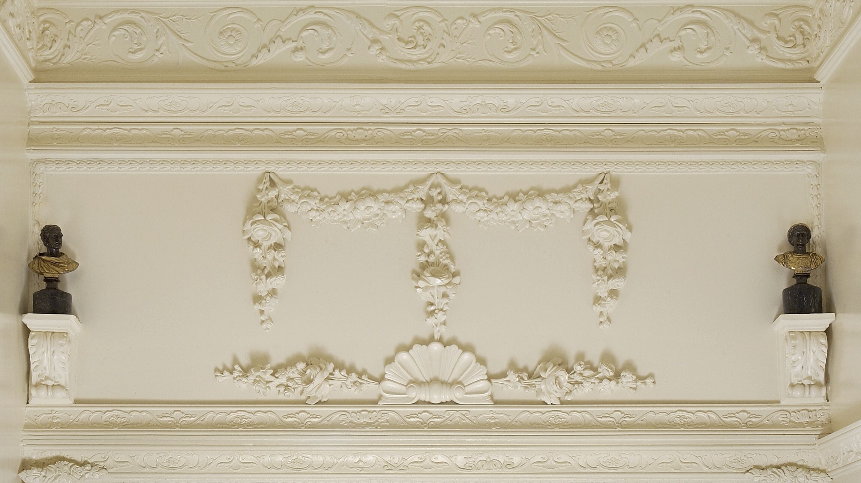 A ceiling with ornate floral and scroll designs, two busts on either side, and a central decorative element.
