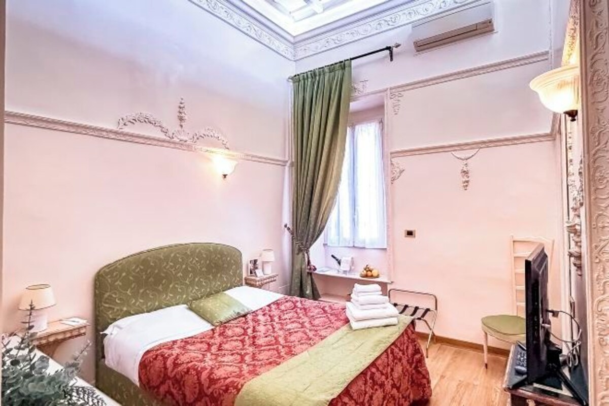 A hotel room with a bed, a desk with a computer, a chair, a television, and a window with curtains.