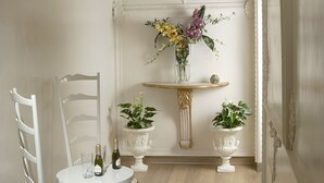A room with a white chair, a small round table with a bottle and glass, and a decorative wall piece. - Suites Rome (Rome)