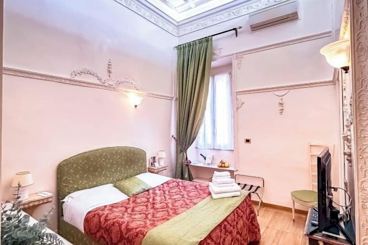A hotel room with a bed, a desk, a chair, a television, and a window with curtains.