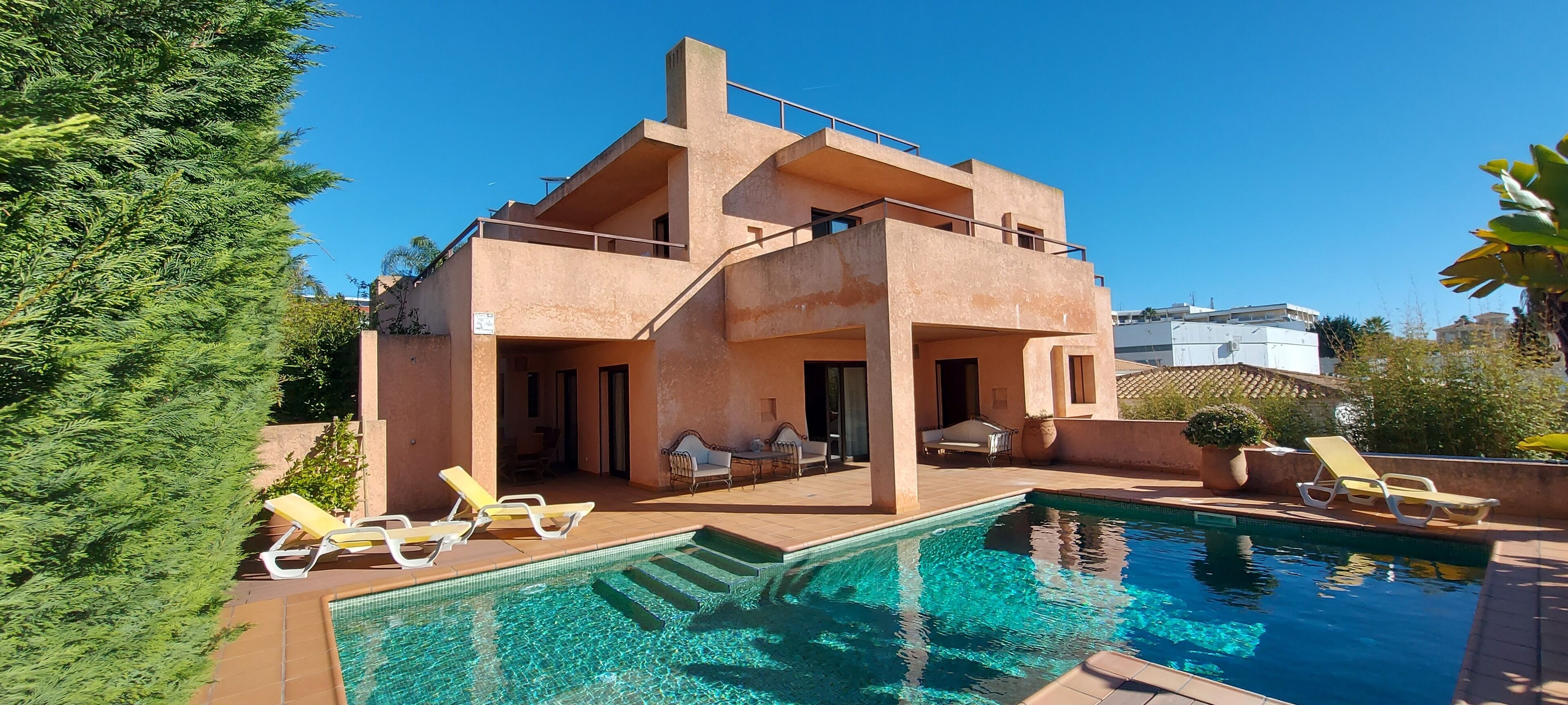 Una casa de dos pisos con piscina y mobiliario de exterior.