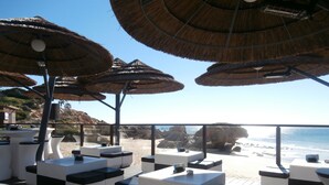 Un salon de plage doté de parasols en chaume, de sièges blancs et confortables, et offrant une vue sur l’océan.