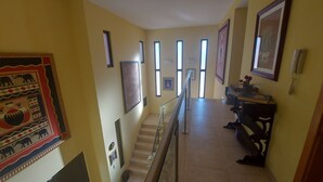 Un couloir avec un escalier, des œuvres d’art encadrées accrochées aux murs et une petite table sur laquelle est posé un vase de fleurs.