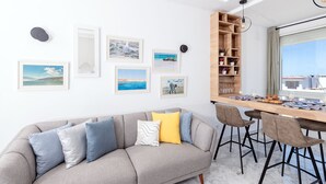 Een moderne woonkamer met een grijze bank, een houten eettafel met stoelen, en een groot raam met uitzicht op de stad.