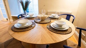 Una mesa redonda para comer con acabado en madera clara, rodeada de individuales tejidos y platos blancos.