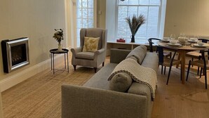 Una sala de estar con un sofá, sillones, una mesa de comedor para cuatro personas y una chimenea.
