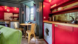 Une cuisine compacte avec un mur d’accent rouge, un lave-linge et un coin repas comprenant une table et des chaises.