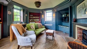 Un salon chaleureux avec un canapé vert, un fauteuil blanc et une cheminée.