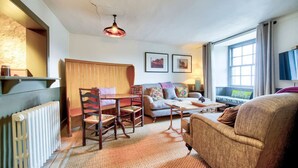 A cozy living room with a wooden dining table, a sofa, and a large window. - The Terrace  · The Rock House: Historic Gem- in Heart of the City (Edinburgh)
