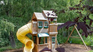 A wooden playhouse with a yellow slide and a swing set in a wooded area. - Idyllic country retreat (Aviemore)