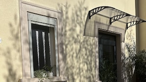 Un edificio con fachada color beige, una escalera que lleva a una puerta y un ventanal con cortina.
