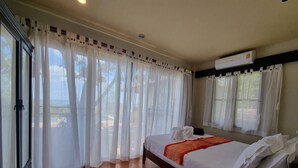 A bedroom with a bed, white curtains, an air conditioning unit, and a view of the outdoors. - Private Pool Villa · Kantiang Bay Sea Views · 3 Bedrooms (Ko Lanta)
