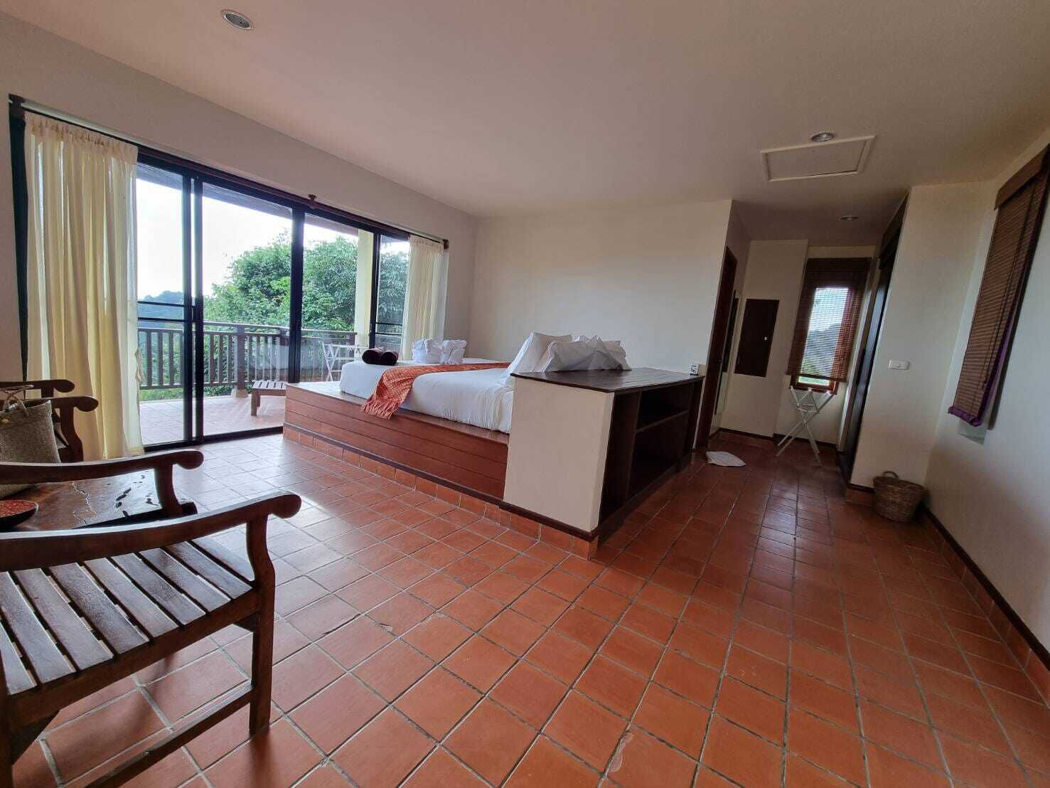 Ein Hotelzimmer mit Bett, Schreibtisch, Stuhl und einem Balkon mit Blick auf Grünflächen.