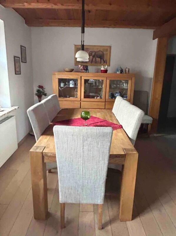 Un comedor con mesa y sillas de madera, un aparador con puertas de cristal y una lámpara colgante.