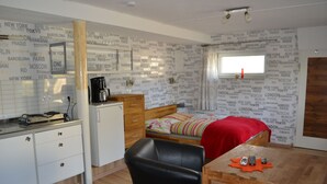 Quarto compacto com cama, escrivaninha, cadeira, mesinha, máquina de café e guarda-roupa.