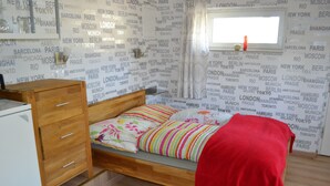 Quarto com cama de madeira, uma pequena escrivaninha e um guarda-roupa.