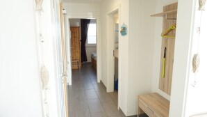 A narrow hallway with a wooden door on the left, a wooden wardrobe on the right, and a bed with a wooden headboard in the background.