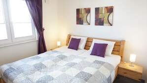 A neatly made bed with a quilt, two pillows, a wooden headboard, and two wall-mounted paintings.