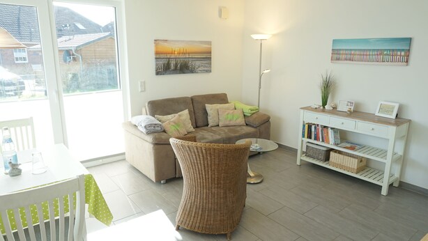 A living room with a sofa, a wicker chair, a coffee table, a bookshelf, and a painting on the wall.