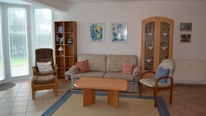 A living room with a sofa, two armchairs, a coffee table, a bookshelf, and a cabinet with glass doors. - Appartement "ordinger Diek" in St. Peter-ording für 2 Personen (St. Peter-Ording)