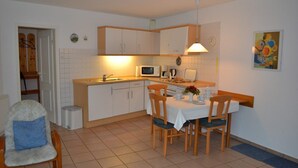 A compact kitchen with white cabinets, a microwave, a sink, and a dining table with chairs. - Appartement "ordinger Diek" in St. Peter-ording für 2 Personen (St. Peter-Ording)