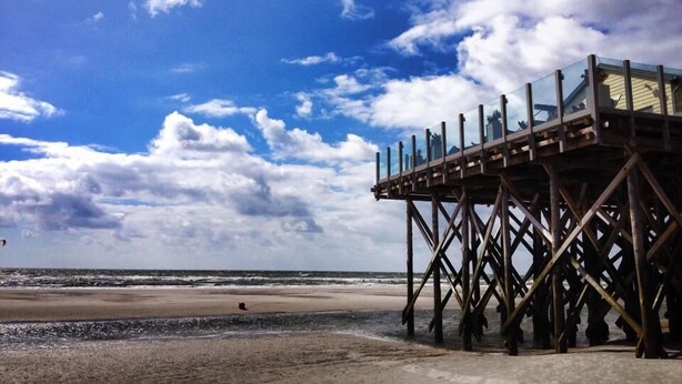 A wooden pier with a glass enclosure overlooking a beach. - Appartement "ordinger Diek" in St. Peter-ording für 2 Personen (St. Peter-Ording)