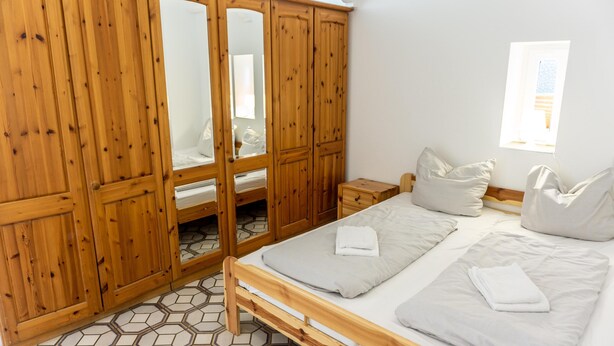 Una camera da letto con un armadio in legno, un letto con cuscini e un pavimento piastrellato.