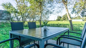 An outdoor dining area with a table and chairs, surrounded by greenery and trees. - Appartement "reiterhof Immensee H" in St. Peter-ording für bis zu 5 Personen (St. Peter-Ording)