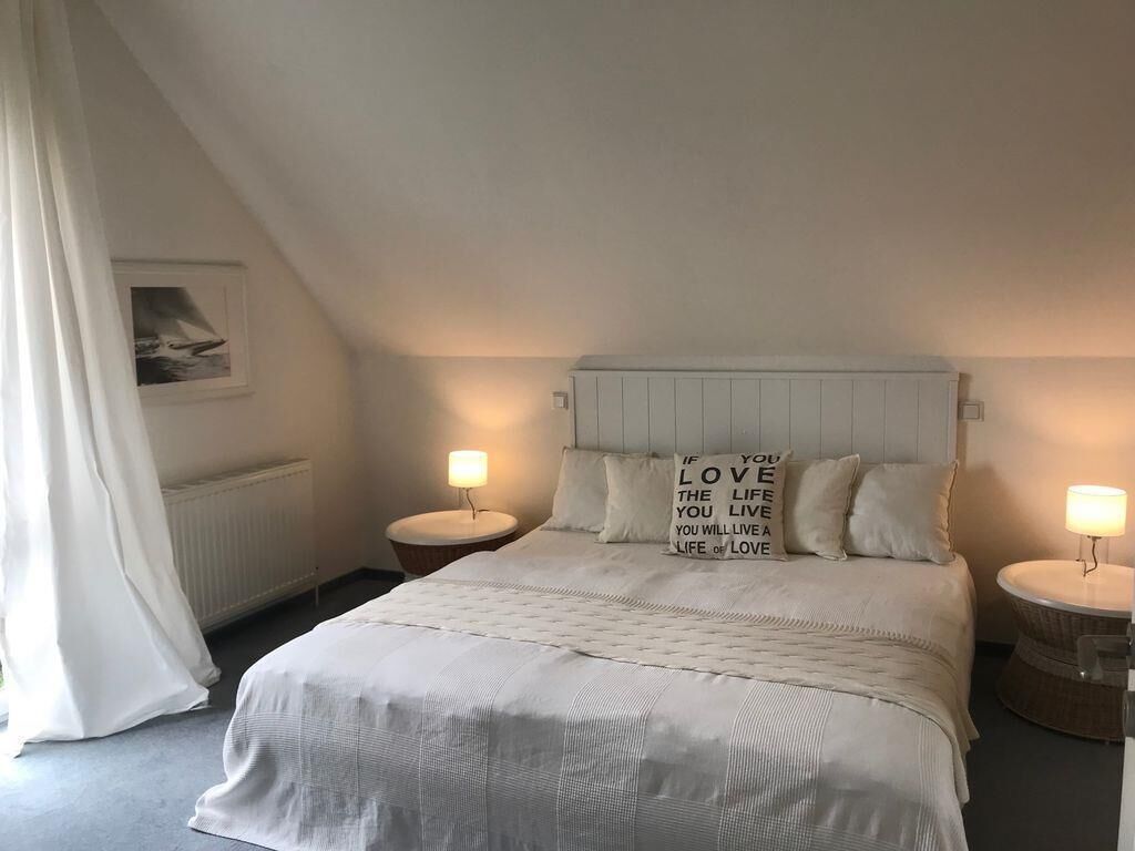 Een keurig opgemaakt slaapkamer met een groot bed, twee nachtkastjes met lampen, en een ingelijst schilderij aan de muur.